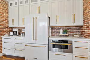 Kitchen with high end fridge, white cabinetry, oven, and brick wall