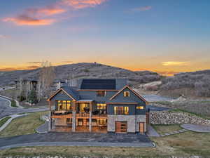 View of front of home with solar panels, a patio area, driveway, stone siding, and a front yard