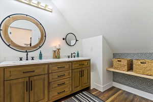 Full bath featuring double vanity, lofted ceiling, wood finished floors, and a sink
