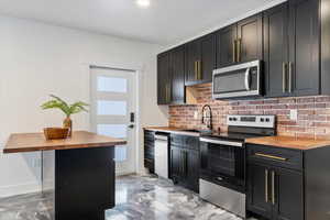 Kitchen with a sink, wooden counters, appliances with stainless steel finishes, and tasteful backsplash