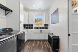 Laundry room featuring dark wood-style floors, washer and clothes dryer, a sink, cabinet space, and visible vents