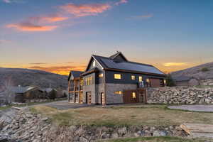 Back of property at dusk featuring stone siding, board and batten siding, roof mounted solar panels, a mountain view, and a yard