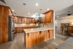 Kitchen featuring wall chimney range hood, a sink, brown cabinets, stainless steel appliances, and a peninsula