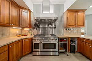 Kitchen featuring brown cabinets, light wood-style floors, wall chimney range hood, and double oven range