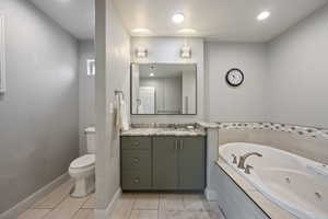 Full bathroom featuring recessed lighting, a whirlpool tub, toilet, vanity, and baseboards