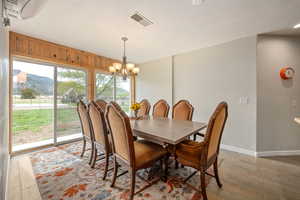 Dining space with light wood finished floors, a wall unit AC, baseboards, visible vents, and a notable chandelier