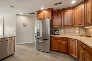 Kitchen with light wood finished floors, stainless steel appliances, visible vents, and brown cabinets