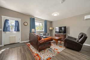 Living room featuring wood finished floors, baseboards, and a wall mounted air conditioner