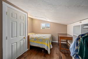 Bedroom with wood-type flooring, lofted ceiling, a textured ceiling, and baseboards