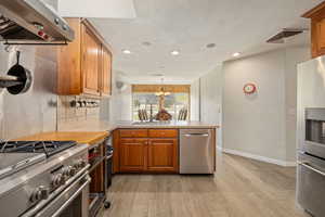 Kitchen featuring ventilation hood, visible vents, light wood-style floors, a peninsula, and appliances with stainless steel finishes