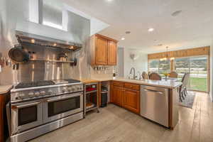 Kitchen featuring wall chimney exhaust hood, stainless steel appliances, a peninsula, and light wood-style floors