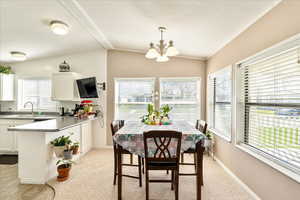 Dining space featuring light carpet, an inviting chandelier, baseboards, and vaulted ceiling with beams