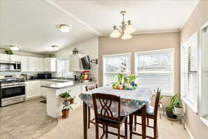 Kitchen with a chandelier, a peninsula, white cabinets, stainless steel appliances, and a sink