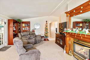 Living area with a glass covered fireplace, lofted ceiling with beams, and light carpet