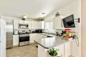 Kitchen featuring stainless steel appliances, a peninsula, white cabinetry, and a sink