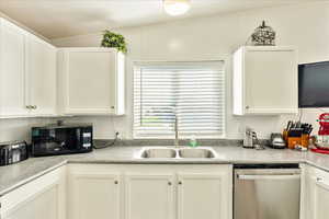 Kitchen featuring black microwave, light countertops, white cabinets, stainless steel dishwasher, and a sink