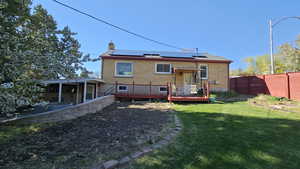Back of house featuring a chimney, a yard, solar panels, a wooden deck, and fence private yard