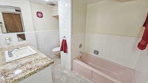 Bathroom with wainscoting, vanity, tile walls, a tub, and toilet