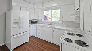 Kitchen featuring white cabinets, a sink, white appliances, light countertops, and under cabinet range hood