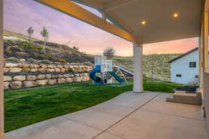 Patio terrace at dusk featuring a yard and a playground