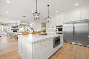 Kitchen featuring a center island, recessed lighting, white cabinetry, built in appliances, and a lit fireplace