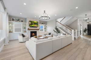 Living room featuring light wood-type flooring, recessed lighting, a chandelier, stairs, and a fireplace