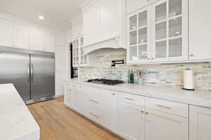 Kitchen with light wood finished floors, white cabinetry, appliances with stainless steel finishes, and tasteful backsplash
