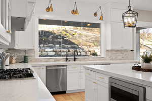 Kitchen featuring backsplash, appliances with stainless steel finishes, a notable chandelier, and a sink