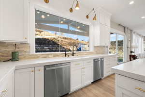 Kitchen with stainless steel dishwasher, a sink, backsplash, white cabinetry, and recessed lighting