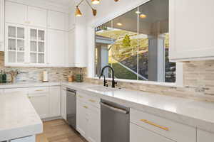 Kitchen featuring light stone counters, stainless steel dishwasher, a sink, decorative backsplash, and white cabinetry