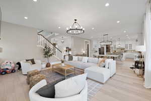 Living room featuring light wood-type flooring, an inviting chandelier, stairs, and recessed lighting