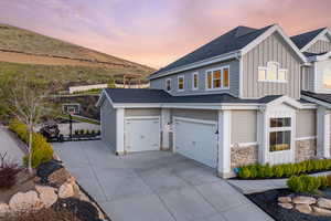 View of front facade featuring driveway, stone siding, board and batten siding, and a garage