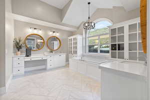 Bathroom with lofted ceiling, a sink, a chandelier, two vanities, and a garden tub