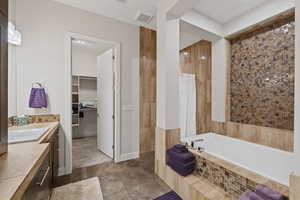 Bathroom featuring a tile shower, visible vents, vanity, a walk in closet, and tiled bath