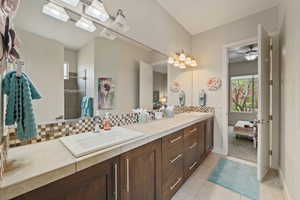 Bathroom with ceiling fan, a sink, backsplash, and double vanity