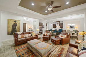 Living area featuring ceiling fan with notable chandelier, baseboards, a tray ceiling, and recessed lighting
