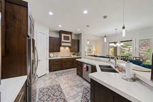 Kitchen featuring stainless steel appliances, a sink, dark brown cabinetry, decorative backsplash, and light countertops