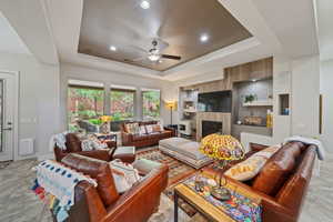 Living area with a tile fireplace, baseboards, a raised ceiling, and ceiling fan