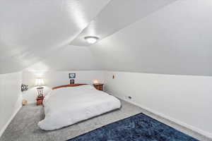 Bedroom featuring lofted ceiling, a textured ceiling, carpet flooring, and baseboards