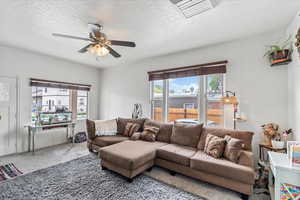 Living area with ceiling fan, carpet floors, and a textured ceiling