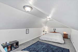 Bedroom with vaulted ceiling, carpet floors, a textured ceiling, and baseboards