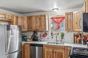 Kitchen featuring stainless steel appliances, light countertops, a sink, and a textured ceiling