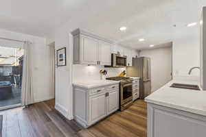Kitchen featuring tasteful backsplash, a sink, appliances with stainless steel finishes, light countertops, and dark wood-style flooring