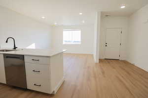 Kitchen featuring a sink, open floor plan, dishwasher, light wood finished floors, and white cabinetry