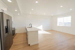 Kitchen with a sink, light wood-type flooring, white cabinetry, light countertops, and appliances with stainless steel finishes