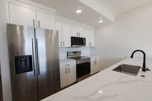 Kitchen with white cabinets, recessed lighting, light stone counters, a sink, and appliances with stainless steel finishes