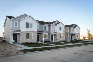 Townhome / multi-family property featuring central AC, stone siding, and a front yard