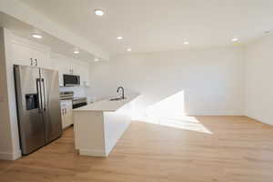 Kitchen featuring a sink, white cabinets, a peninsula, appliances with stainless steel finishes, and recessed lighting