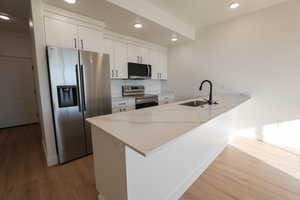 Kitchen featuring recessed lighting, wood finished floors, a sink, a peninsula, and appliances with stainless steel finishes
