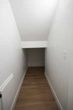 Hall with wood finished floors, lofted ceiling, and baseboards